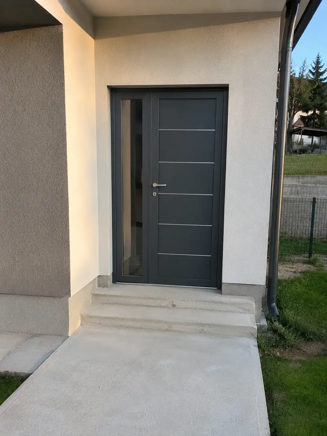 Nova kuća sa antracit ulaznim vratima i betonskom stazom do ulaza